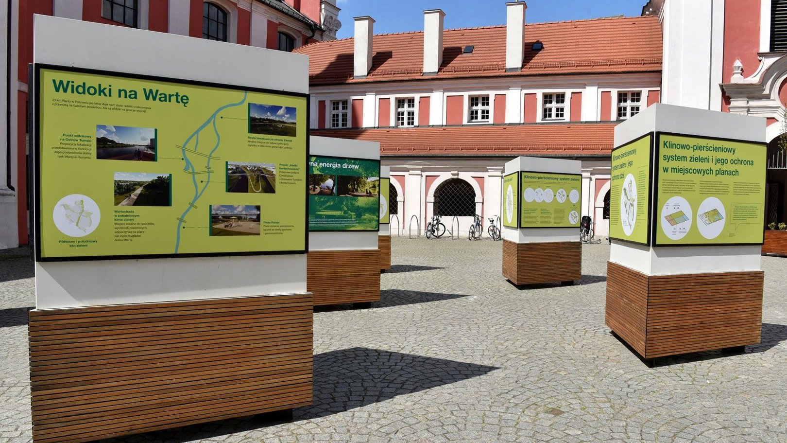 Na zdjęciu zielone plansze wystawy, w tle budynek urzędu, przed nim rowery
